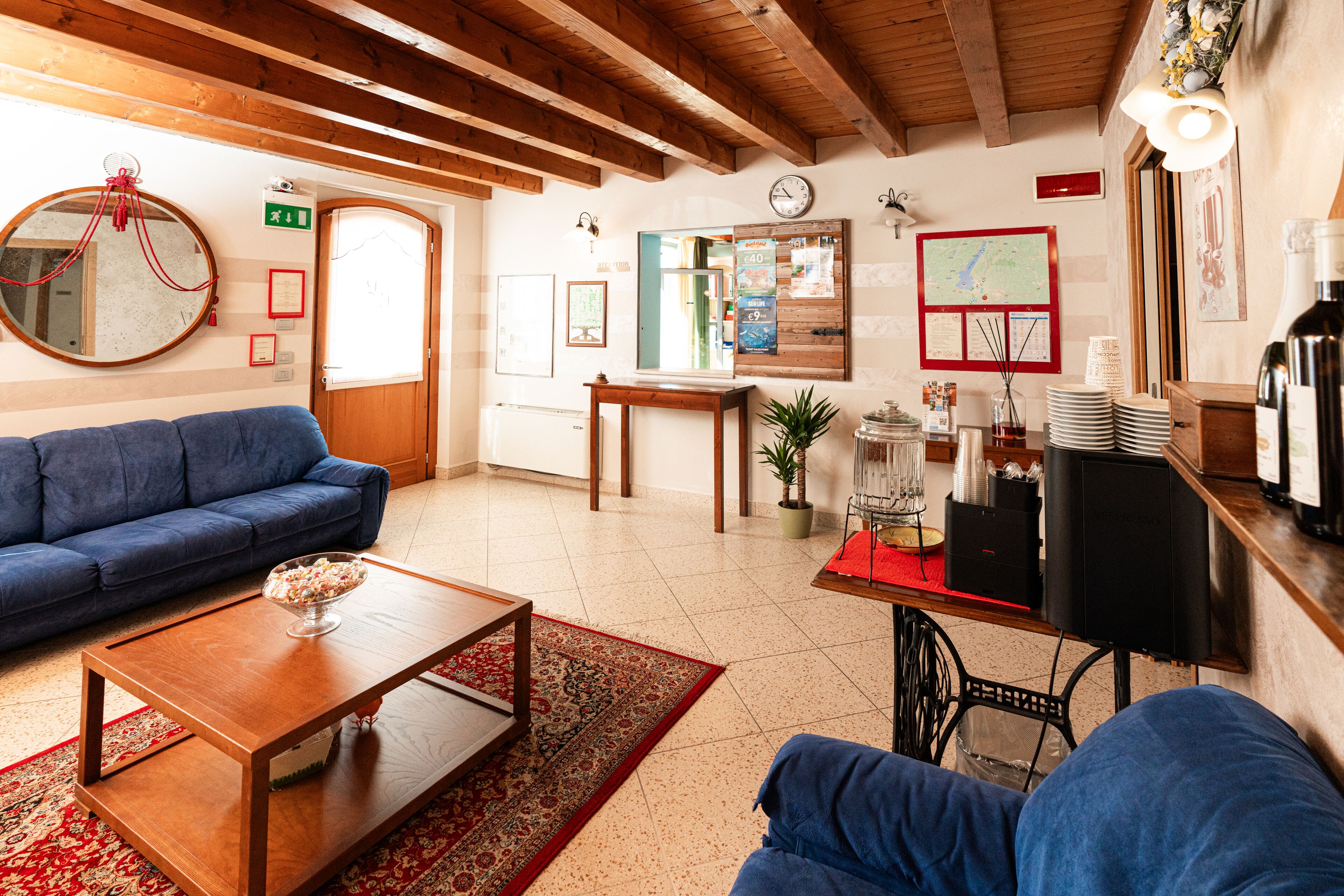 A cozy living area with a blue sofa, wooden coffee table, and a red-rugged floor. A wooden ceiling and a wooden-framed mirror are also visible.