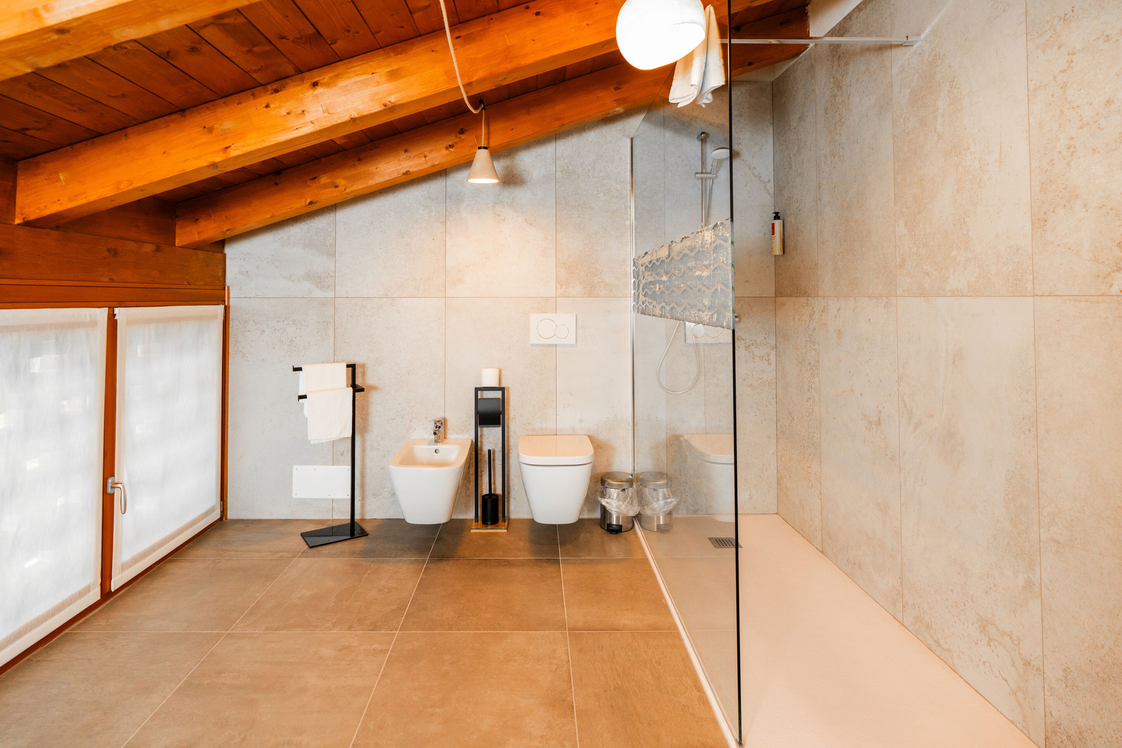 Un baño moderno con techo de madera, cabina de ducha de vidrio y lavamanos blanco.