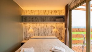 A bedroom with a large bed, wooden headboard, two bedside tables, and a view of the outdoors through a large window.