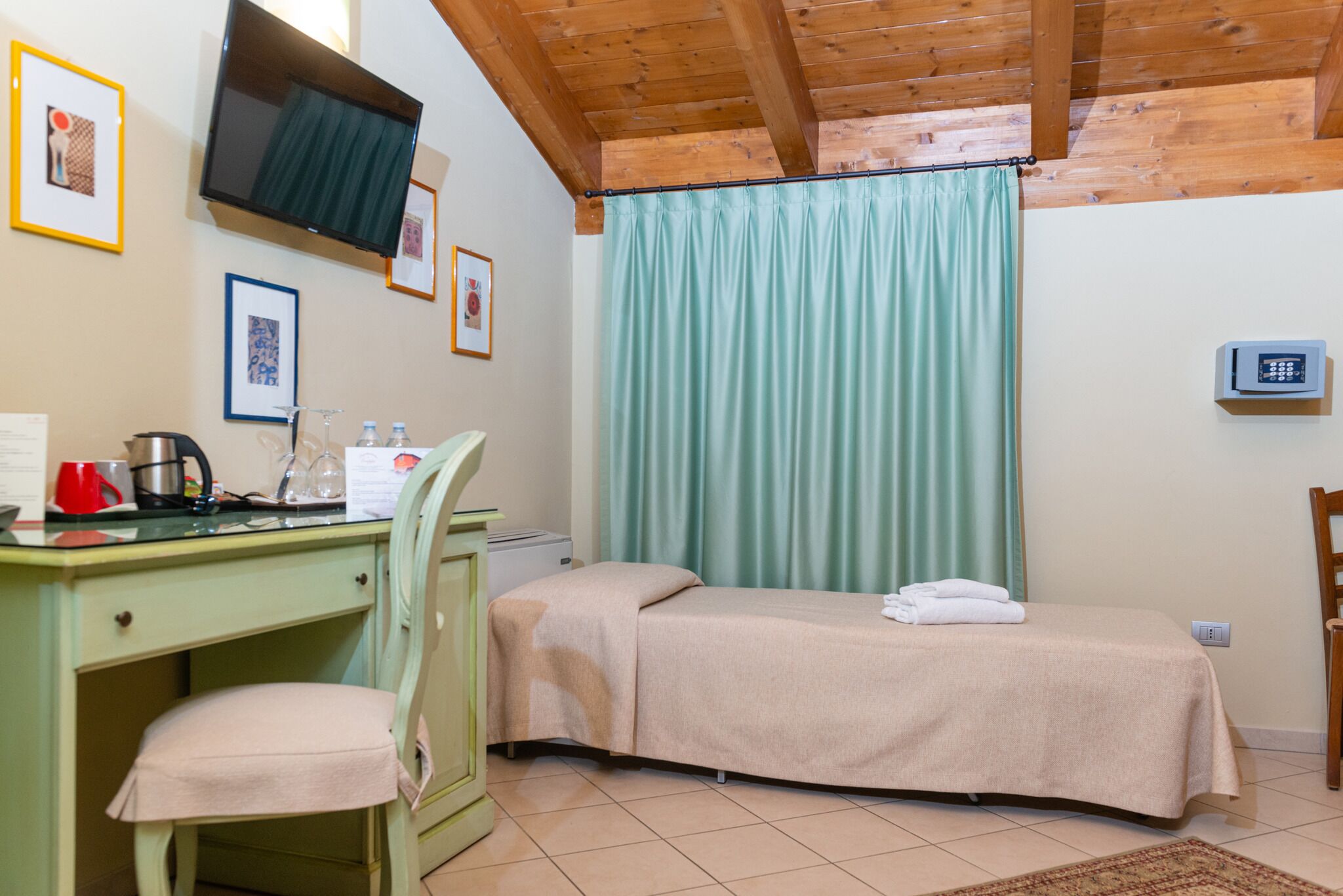 A room with a bed, a desk with a chair, a TV mounted on the wall, and a window with curtains.