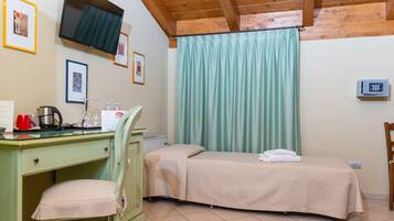 A room with a bed, a desk with a chair, a TV mounted on the wall, and a window with curtains.