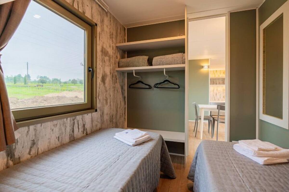 A bedroom with two beds, a window, a closet with shelves, and a desk area.