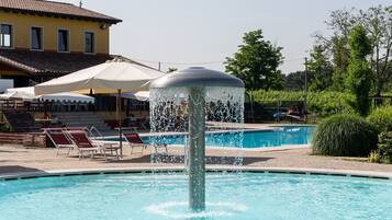 Une piscine avec une fontaine, des chaises longues et, au fond, un bâtiment doté d’un toit recouvert de tuiles.