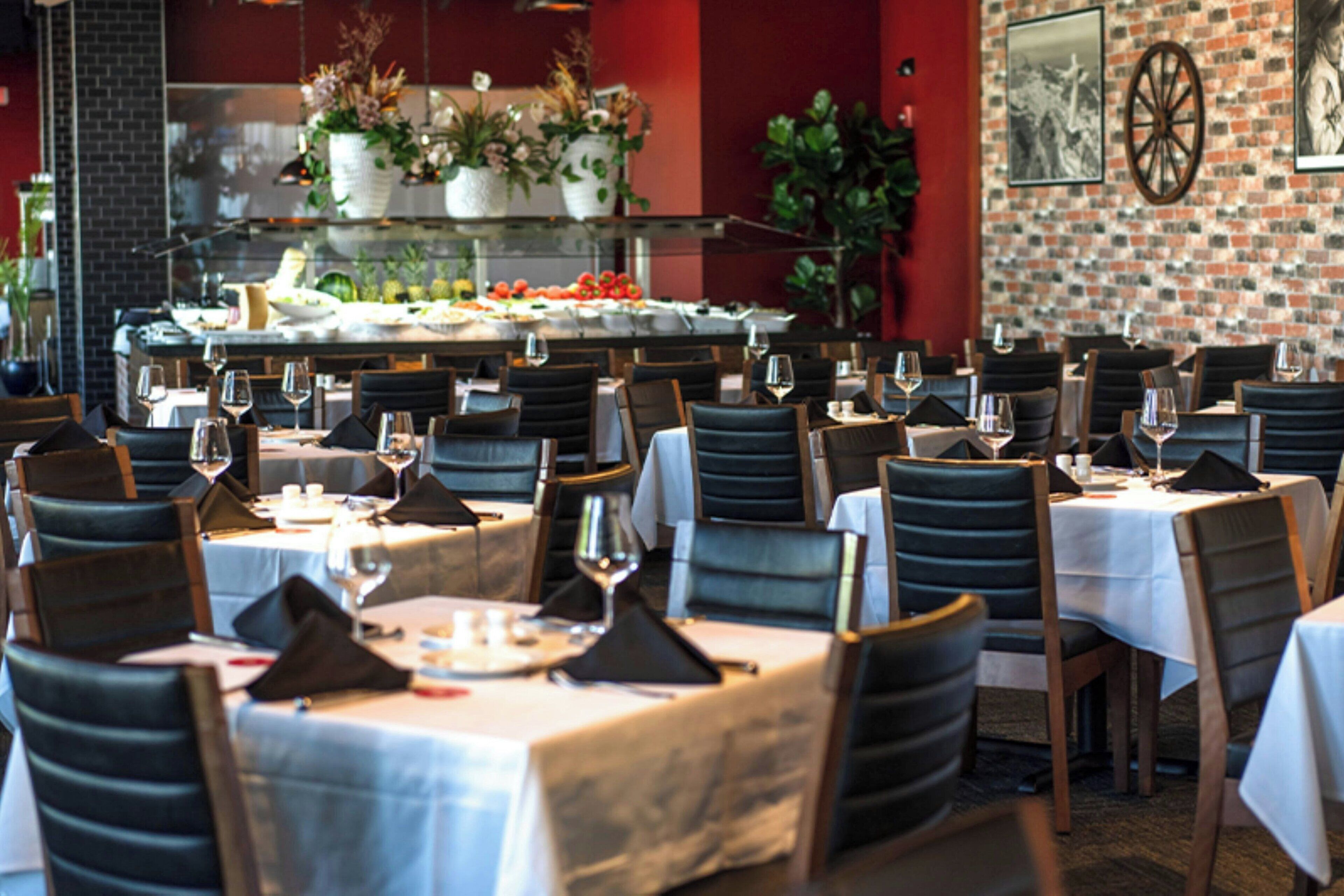 Een restaurant met meerdere tafels en stoelen, elk voorzien van wijnglazen en servetten.