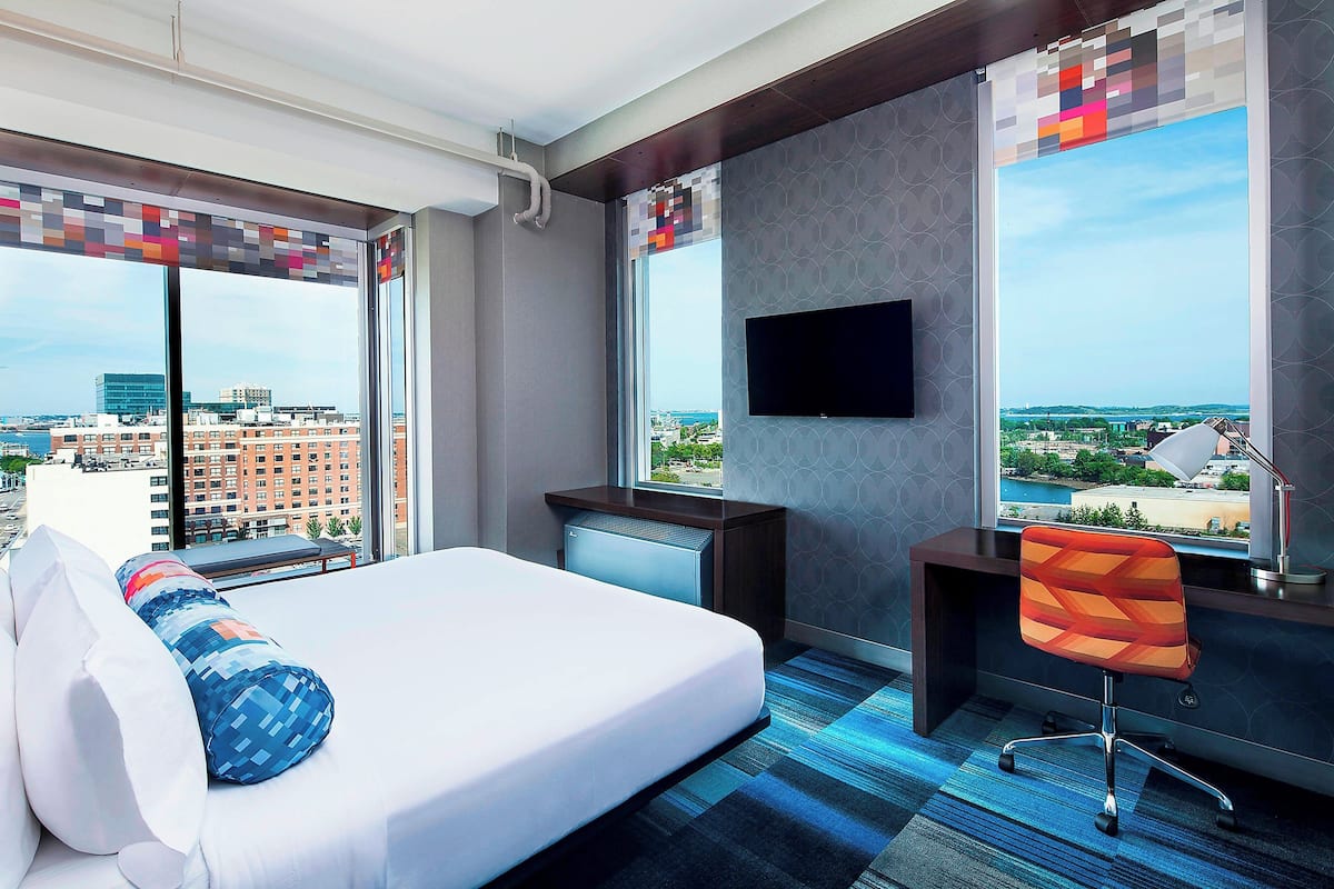 A hotel room with a bed, a desk, a chair, and a TV mounted on the wall.