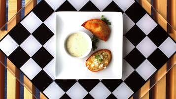 A white plate with two pastries and a small bowl of sauce on a checkered tablecloth.