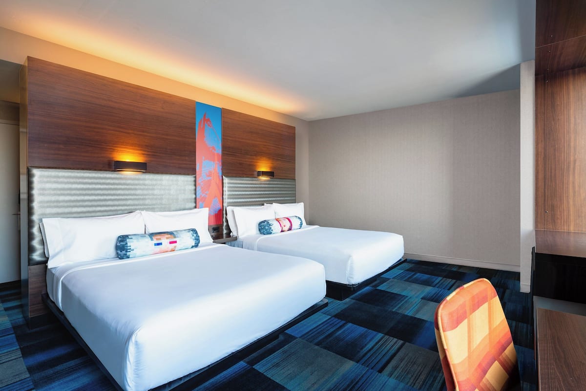 A hotel room with two beds, a large wall art piece, and a patterned carpet.