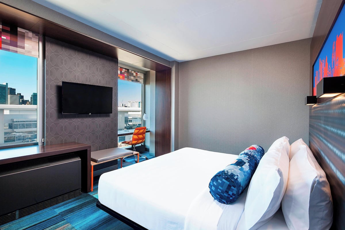 A hotel room with a bed, a desk, a chair, a TV, and a city view.