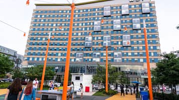 A modern hotel with a glass facade, multiple floors, and a prominent orange vertical structure in front.
