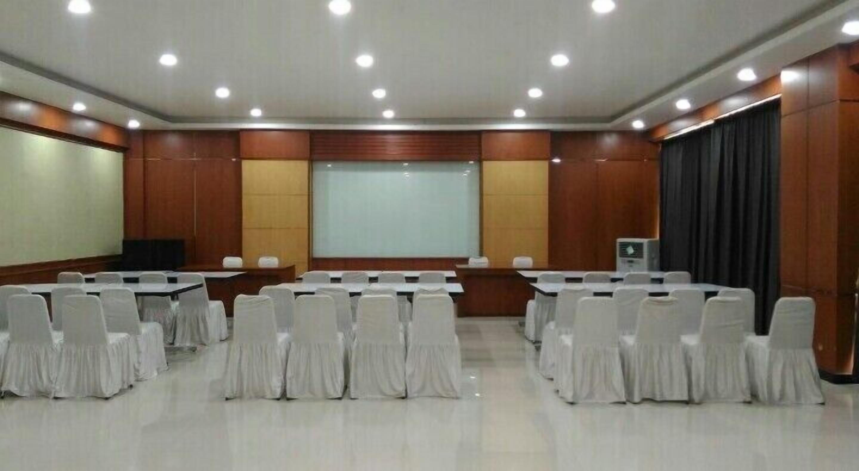 A conference room with rows of tables and chairs, a projector screen, and a podium.