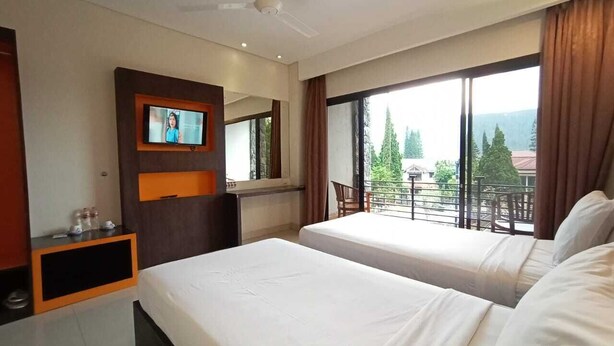 Habitación de hotel con dos camas, un televisor montado en la pared, un balcón con vistas a árboles y edificios, y un ventilador de techo.