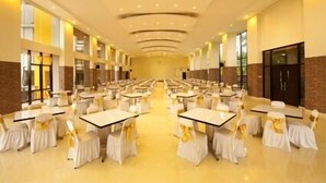 Un amplio salón de banquetes con filas de mesas y sillas, ventanas grandes y un diseño moderno en el techo.