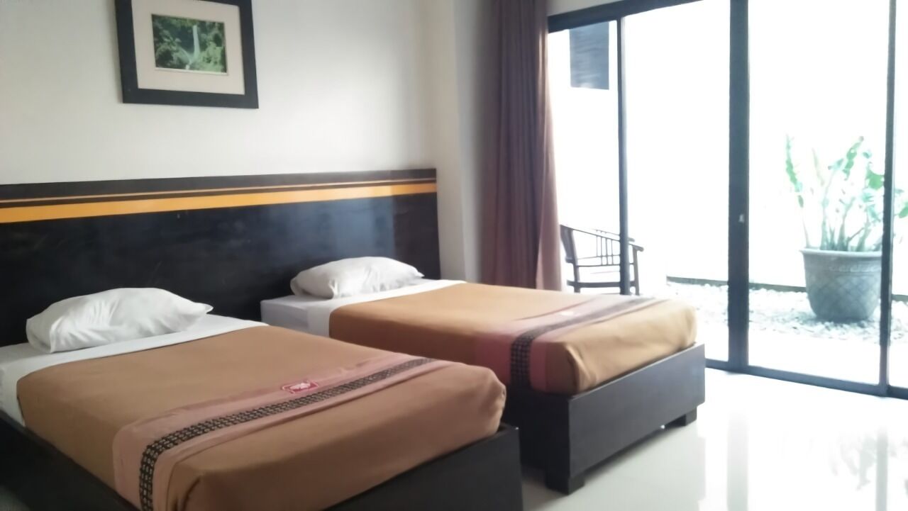 A hotel room with two beds, a large window, and a balcony with a potted plant.