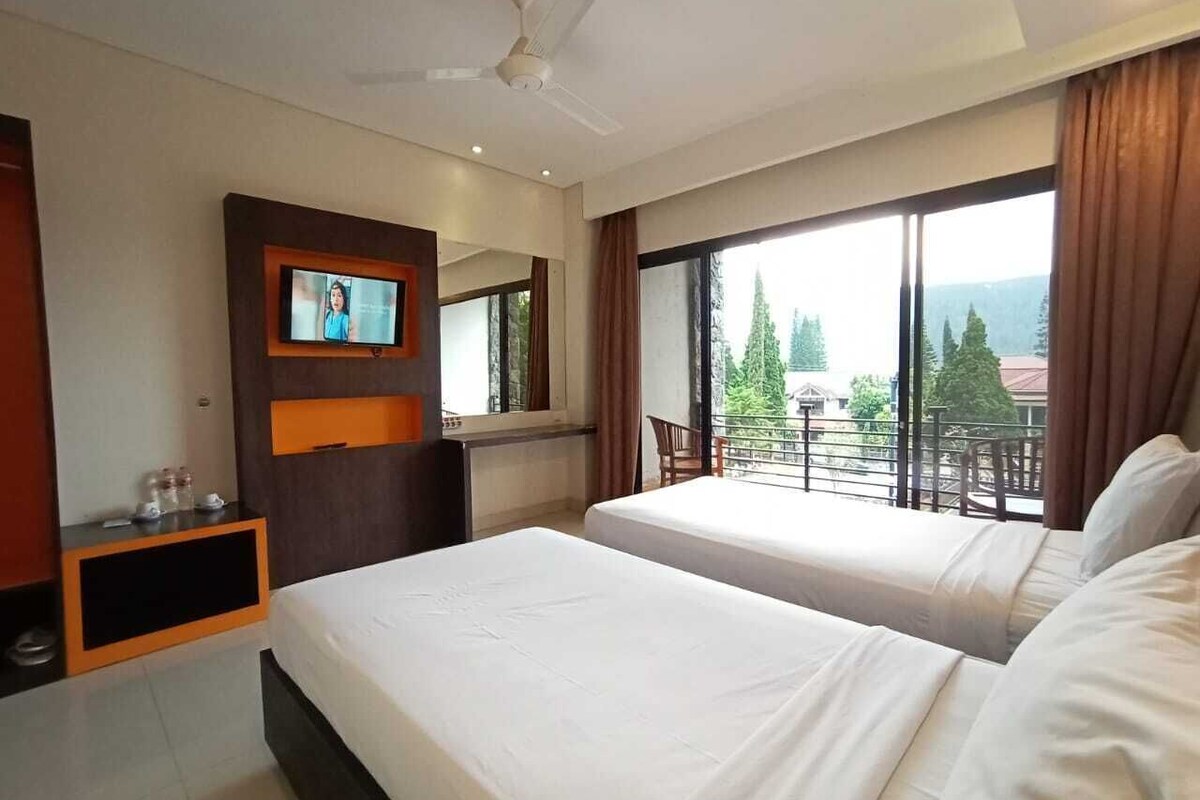 Habitación de hotel con dos camas, televisor montado en la pared, balcón con vistas y ventilador de techo.