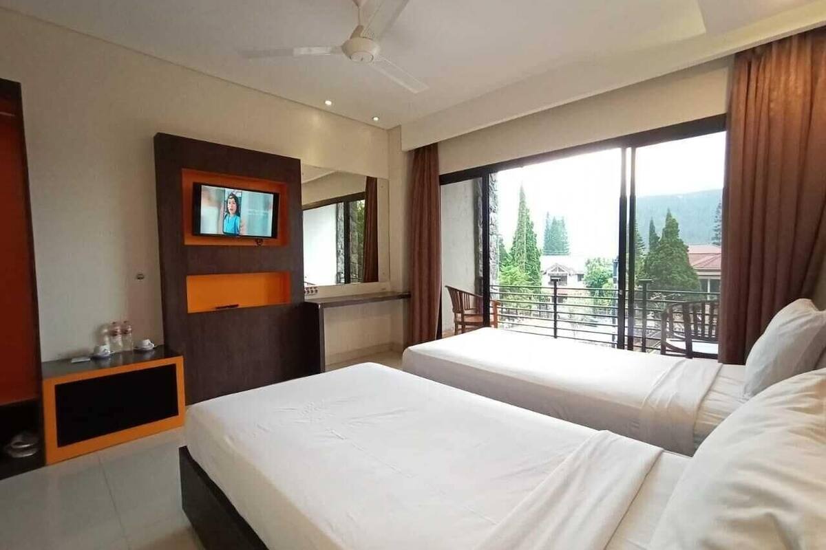 Een hotelkamer met twee bedden, een aan de muur bevestigde televisie, een balkon met uitzicht en een plafondventilator.