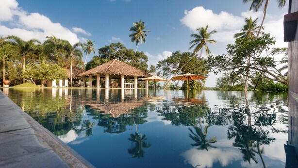 A pool with a reflection of palm trees and a building with a tiled roof. - Kahanda Kanda (Angulugaha)