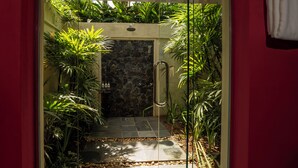 A glass-enclosed shower area with a stone wall, surrounded by lush greenery. - Kahanda Kanda (Angulugaha)