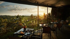 An outdoor dining area with tables and chairs, overlooking a lush landscape with palm trees and a sunset view. - Kahanda Kanda (Angulugaha)