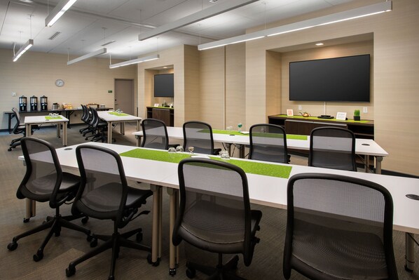 A conference room with multiple tables and chairs, a large screen, and a clock on the wall.