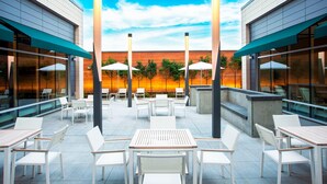 An outdoor patio area with tables and chairs, large umbrellas, and a view of a sunset through a glass wall. - Element by Marriott Boston Seaport District (Boston)