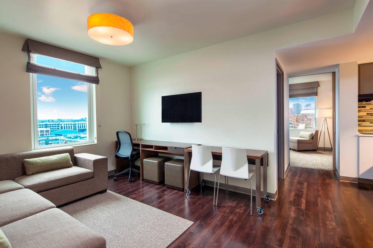 Un salon moderne avec un canapé, un bureau et des fauteuils, un téléviseur à écran plat et une vue sur la ville.