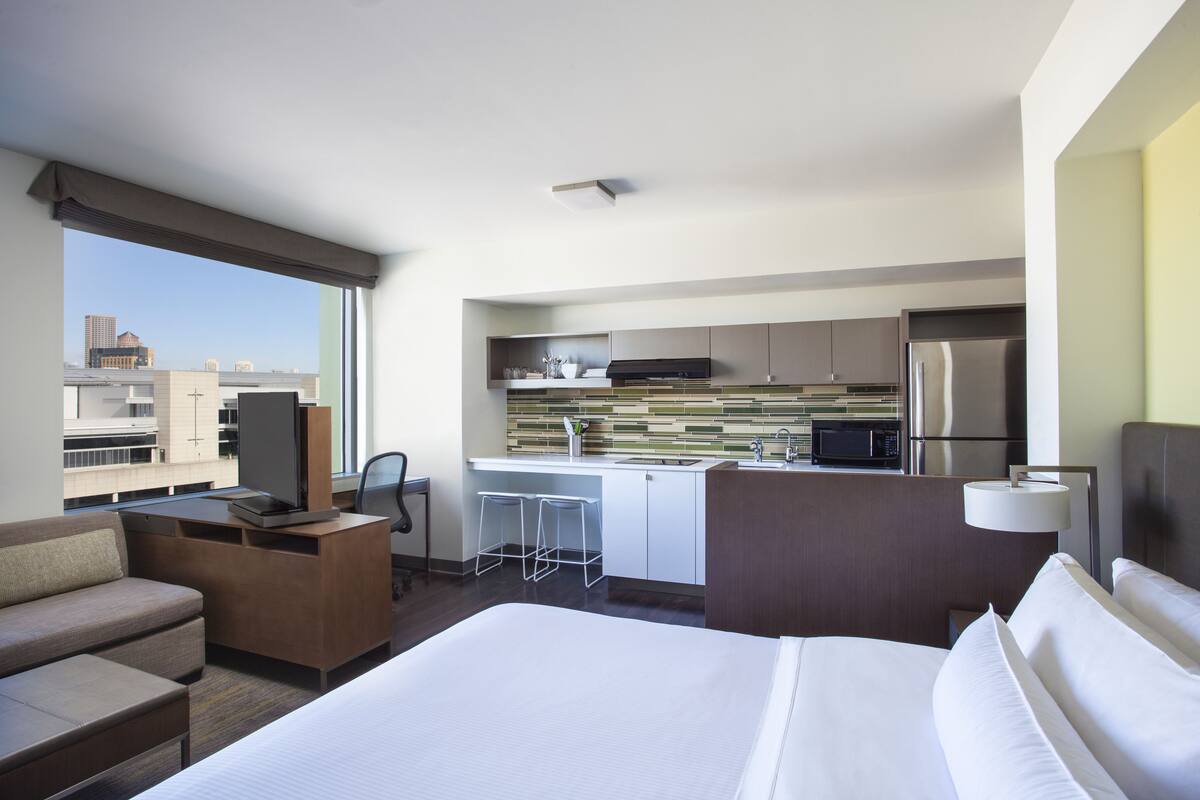 Une chambre d’hôtel équipée d’un lit, d’un bureau, d’une kitchenette et offrant une vue sur la ville.