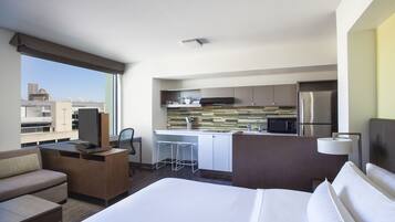 Habitación de hotel con cama, escritorio, kitchenette y vistas a la ciudad.