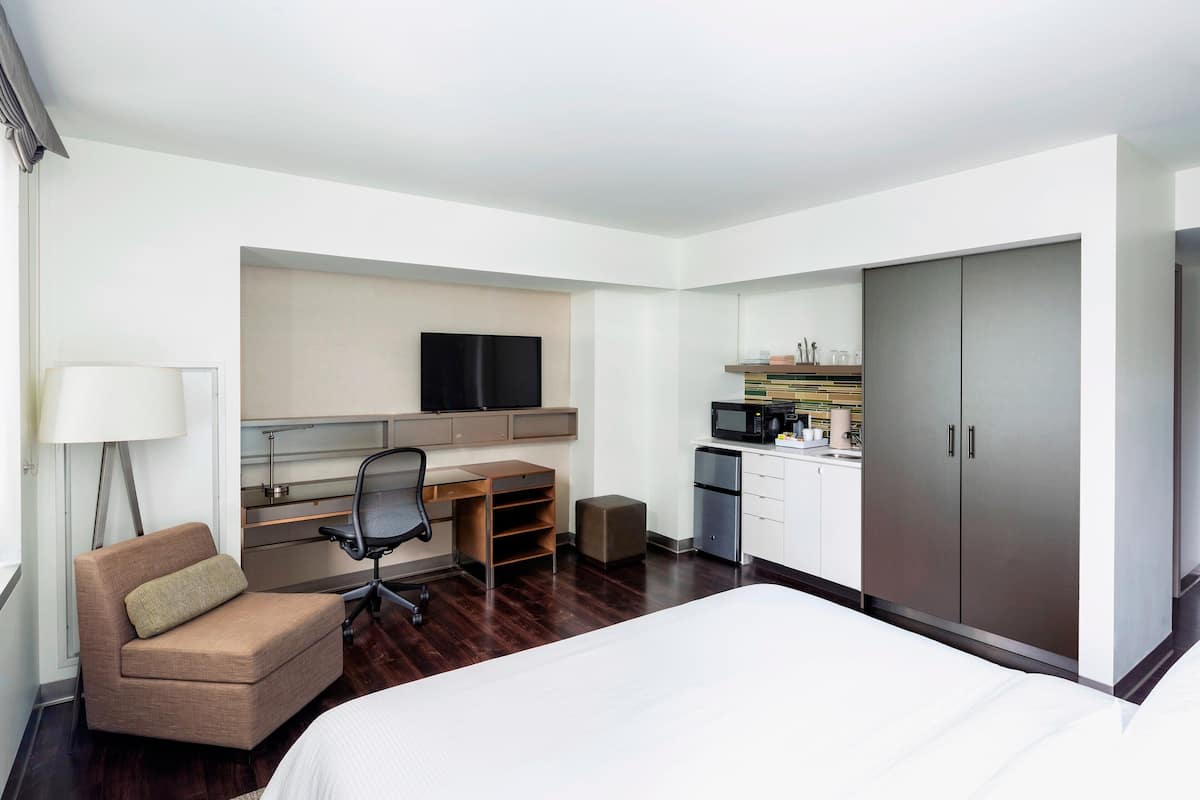 Une chambre d’hôtel comprenant un lit, un bureau avec une chaise, une télévision, une kitchenette et une armoire.