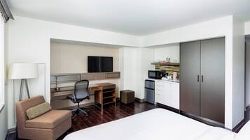 A hotel room with a bed, a desk with a chair, a television, a kitchenette, and a wardrobe.