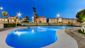 Una piscina con borde de azulejos, rodeada por un muro de piedra bajo y palmeras.