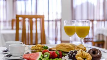 Ein Frühstückstisch mit Tellern voller Obst, Gebäck und zwei Gläsern Orangensaft.