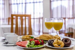 Desayuno con platos de frutas, pasteles y dos vasos de jugo de naranja.