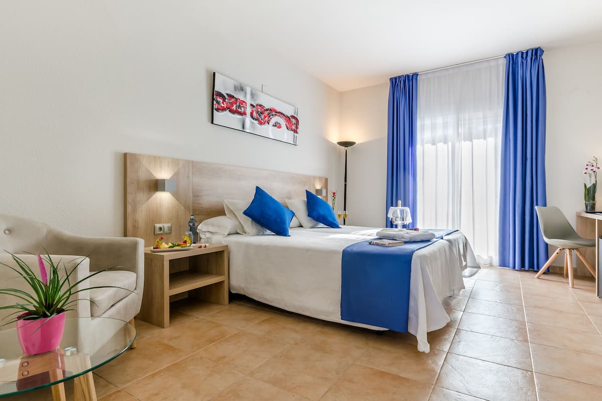 A modern hotel room with a bed, a sofa, a small table, and a potted plant.