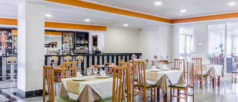 Un restaurante espacioso con varias mesas y sillas, una zona de bar y vistas al exterior.