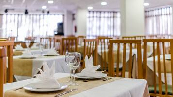 A dining area with tables set for service, featuring white tablecloths, neatly folded napkins, and empty wine glasses.
