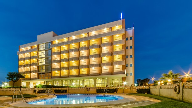 Un hotel de varios pisos con una piscina delantera.