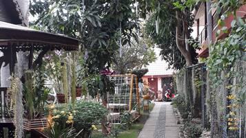 Stroll through the serene garden, surrounded by lush greenery and vibrant flowers, leading to a charming building with a red facade.