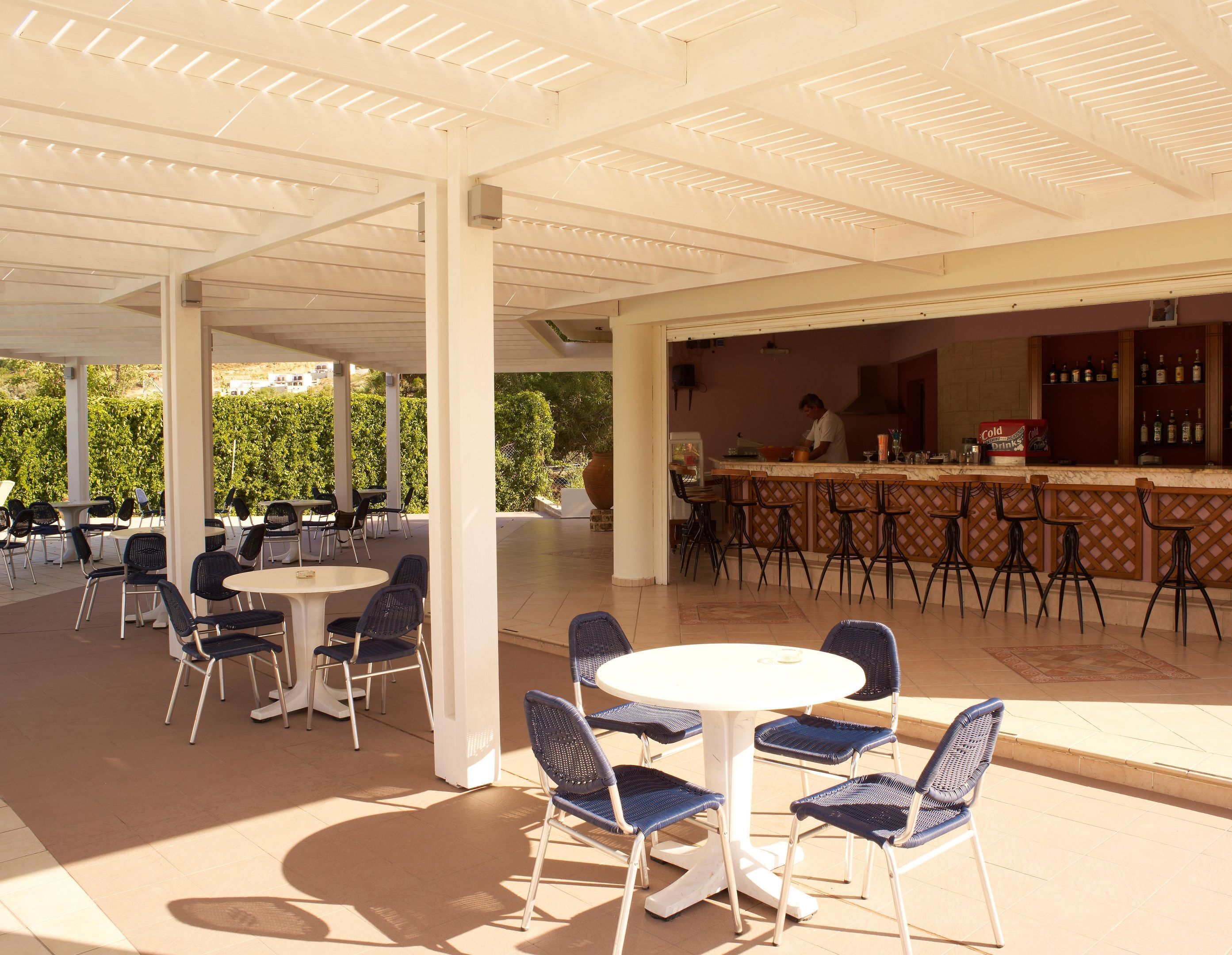 An outdoor patio area with round tables and chairs, a bar with stools, and a chef preparing food.