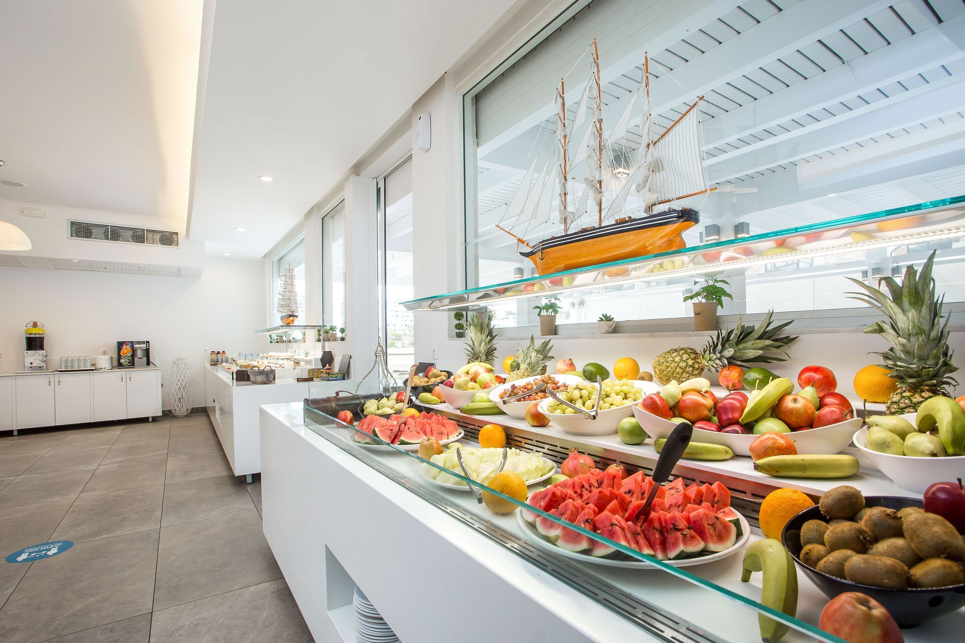A buffet with a variety of fruits and vegetables, a ship model, and a modern kitchen area in the background.