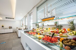 Un bufé con una variedad de frutas y verduras, un modelo de barco y una cocina moderna al fondo.