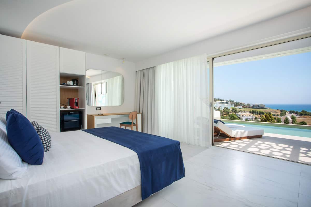 A hotel room with a bed, a desk, a chair, a large mirror, and a view of the ocean.