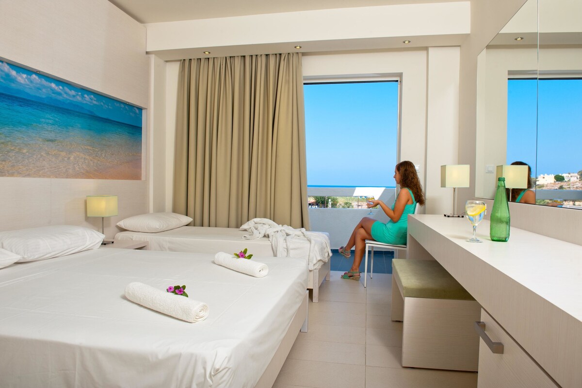 A hotel room with a bed, a desk, a chair, a window with a view, and a painting on the wall.