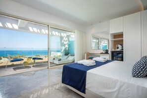 A modern hotel room with a balcony overlooking the sea, a bed with blue bedding, a desk with a chair, and a wardrobe. - Lindos White Hotel & Suites (Rhodes)