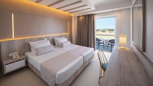 A hotel room with a large bed, bedside tables, a desk, a chair, a balcony with a view, and a large mirror. - Lindos White Hotel & Suites (Rhodes)