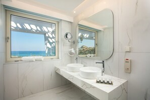 A modern bathroom with two sinks, a large mirror, and a window with a view of the ocean. - Lindos White Hotel & Suites (Rhodes)