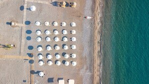 An aerial view of a beach with rows of umbrellas and lounge chairs, a wooden walkway, and a lifeguard tower. - Lindos White Hotel & Suites (Rhodes)