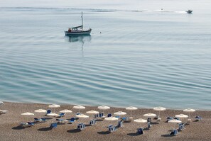 Una playa con hileras de sombrillas y sillas, un bote en el agua y un mar tranquilo.