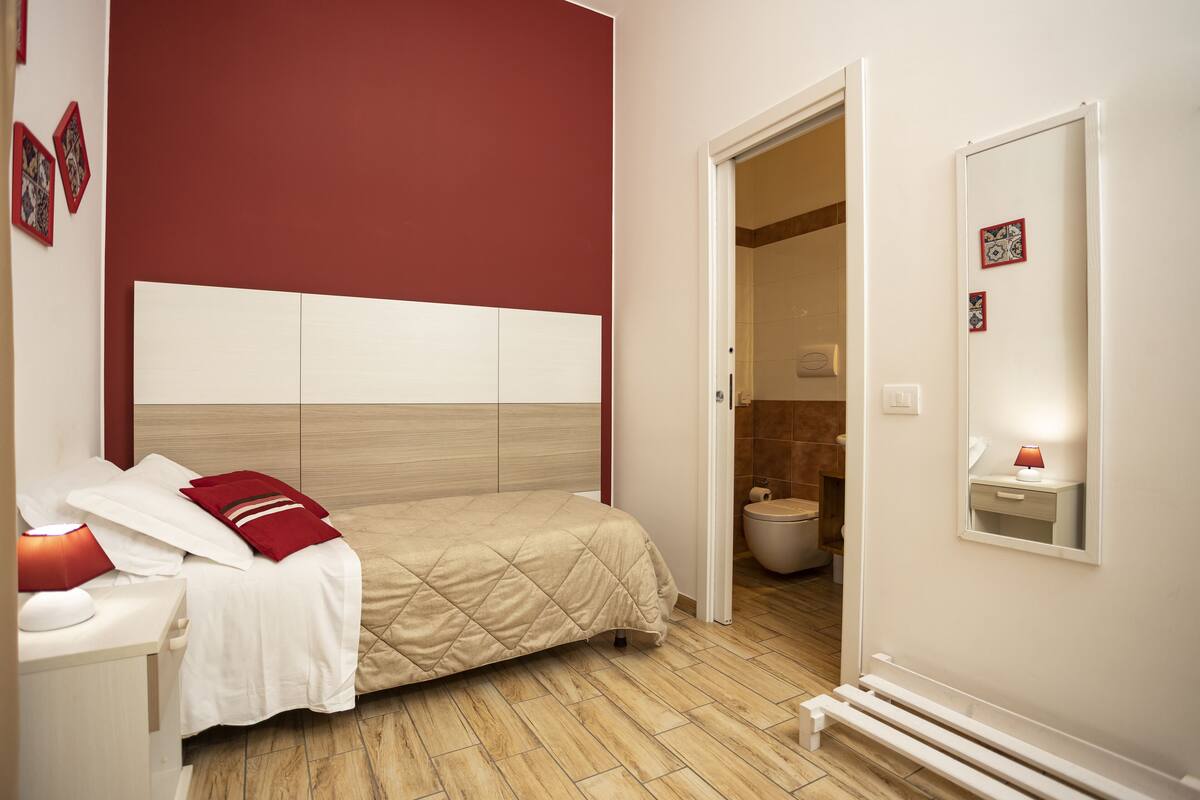 Una habitación de hotel con cama, mesita de noche y baño visible a través de una puerta abierta.