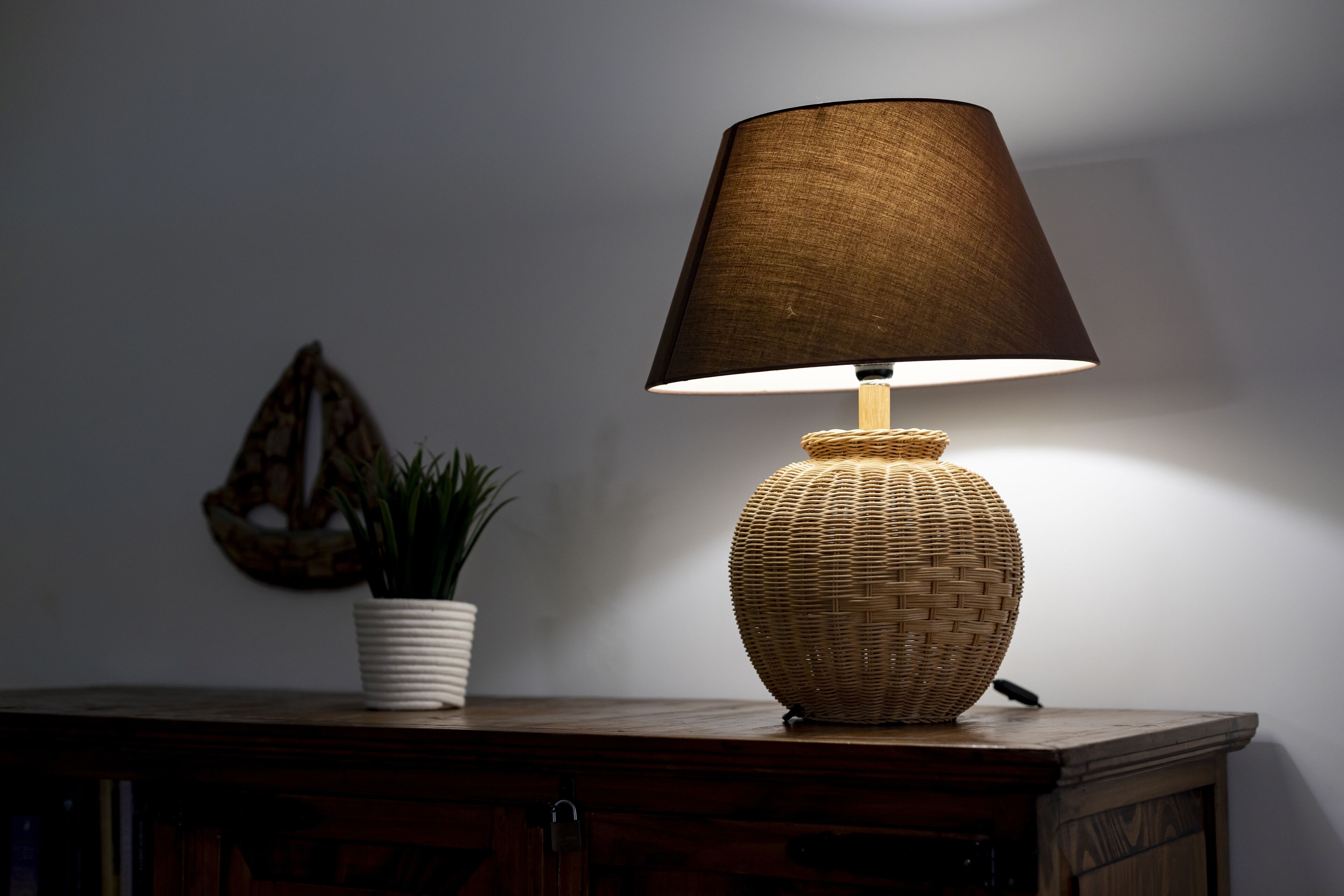 A lamp with a woven base and a dark shade on a wooden surface.