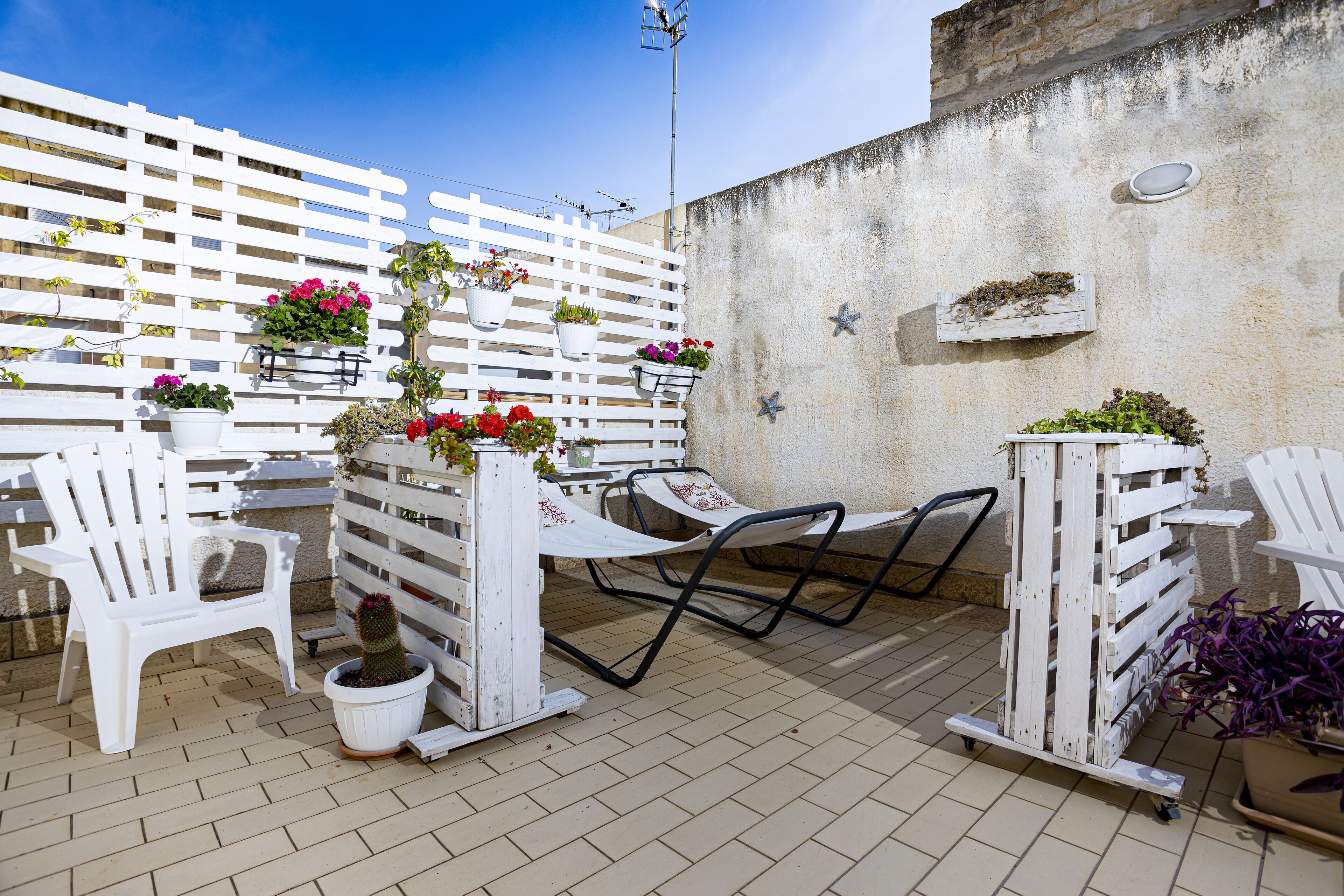 A patio area with white chairs, a table, and potted plants.